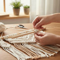 Person crafting a macrame Wand hängende mit Holz Holzstäbe auf einer Holz table mit a soft, blurred background.